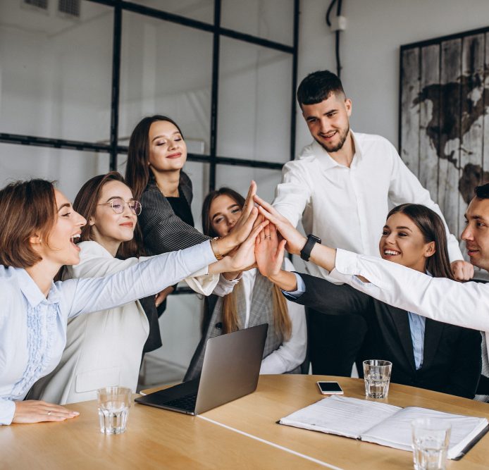 Équipe en réunion célébrant un succès, se donnant un high-five autour d'une table.